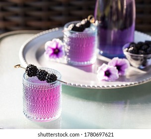 Blackberry Mocktail With Blackberry Skewer And A Tray Of The Same In Soft Focus In Behind.