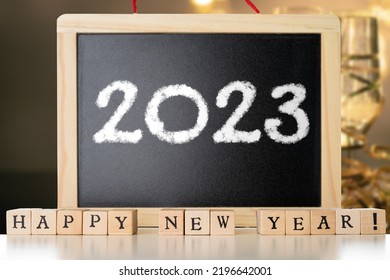 Blackboard with 2023 chalk text and happy new year made of wooden blocks witg festive champagne in the background. New Year's Eve concept
