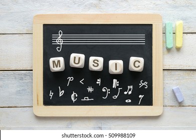 Blackboard In A Classroom With Some Notation Symbols. Some Wooden Cube Letters Composing The Word MUSIC. Empty Copy Space For Editor's Text.