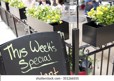 A Blackboard In Front Of A Cafe In Chicago, Illinois Mentioning The Special Menu Of The Week. On The Background, People Are Seen Having Their Food In The Restaurant.