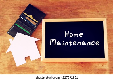 Blackboard With The Phrase Home Maintenance Written On It Over Wooden Board With Wallet, Credit Cards 