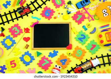 Blackboard Surrounded By Many Different Children's Toys And Numbers On Yellow Background. Early Childhood Education Concept, Preschool