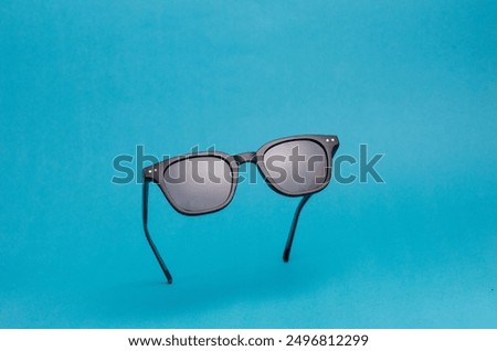 Black-doff rectangular sunglasses on blue background. Minimalist product display concept.