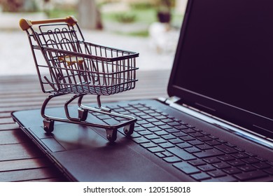 Blackfriday And Cybermonday. Small Trolley With A Black Computer On A Wood Table. Shopping Online And E-commerce Concept. Buy Gifts On Internet.