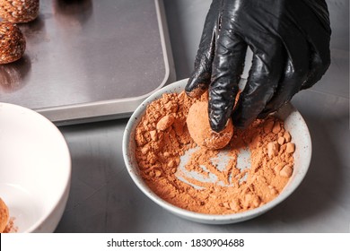 A Black-gloved Cook Prepares Date Sweets And Rolls Them In A Carob.