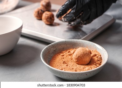 A Black-gloved Cook Prepares Date Sweets And Rolls Them In A Carob.