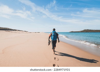 Black-haired good-natured man with a backpack and shoes in his hands walks along the beach of Praia da Ilha do Pessegueiro on the Atlantic Ocean near Porto Covo, Portugal. Fisherman Trail. - Powered by Shutterstock