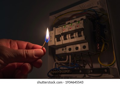 Blackout concept. Person's hand in complete darkness holding a burning match to investigate a home fuse box during a power outage.