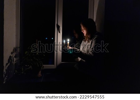 Blackout. Energy crisis. Destruction of infrastructure. Power outage concept. Girl with a burning candle in a dark room sits near the window