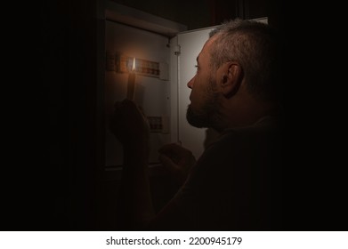 Blackout, No electricity. A man with a candle in the dark examines the electrical switchboard at home during a power outage. - Shutterstock ID 2200945179