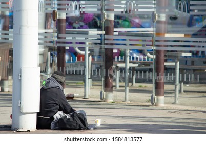 Blackpool, Lancashire/UK - October 12th 2019: Homeless Unemployed Beggar Sat On Street Begging With Paper Cup Outside McDonalds