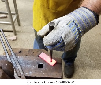 Blacksmith drifting a hole into steel at an anvil wearing a leather apron and work gloves. - Powered by Shutterstock