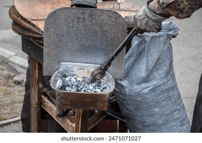 Blacksmith are engaged in the ancient еraditional craft of blacksmithing deftly manipulate metal tongs lifting glowing embers from a bed of hot coals - Powered by Shutterstock