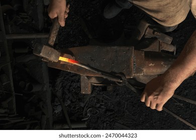 Blacksmith forges a red-hot metal piece on an anvil in a rural forge. Traditional crafts . top view - Powered by Shutterstock