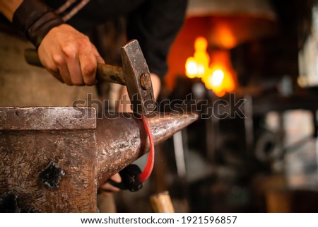 A blacksmith forging horseshoe with hammer. blacksmith forges a horseshoe in a forge on an anvil A forging furnace with fire at background.