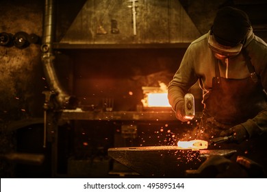 The blacksmith forging the molten metal on the anvil in smithy.