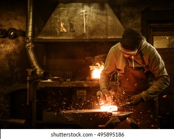 The blacksmith forging the molten metal on the anvil in smithy.