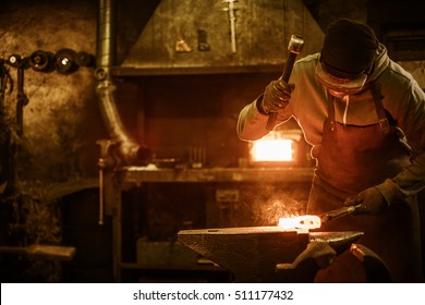 Blacksmith forging the molten metal on the anvil in smithy.