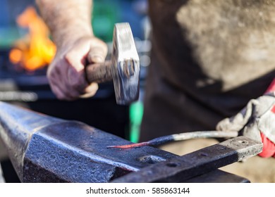 Blacksmith Hammering Red Hot Iron Rod On Anvil Against The Background Of Fire