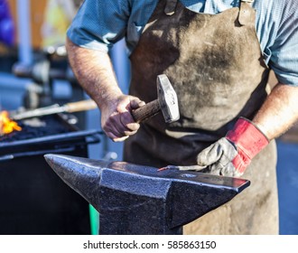 Blacksmith Hammering Red Hot Iron Rod On Anvil Against The Background Of Fire