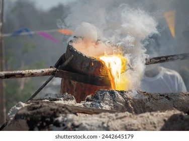 Blacksmith holding a hot crucible by the iron pliers from furnace and pouring the melting gold into the statue block. The process to making of metal statue in local Thailand traditional. - Powered by Shutterstock