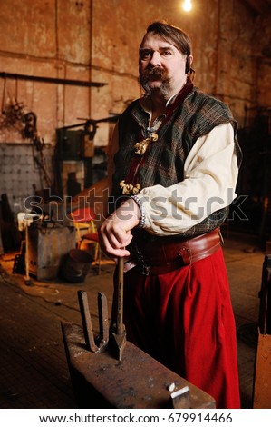 Blacksmith Kozak or a Cossack in Ukrainian national clothes with a hammer in the hands on the background of a blacksmith shop