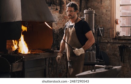 Blacksmith, man and fire with metal rod, flame and equipment for professional craft. Protection, apron and gloves in workshop with anvil for metalwork, hammer and forge for iron product creation - Powered by Shutterstock