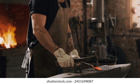 Blacksmith, man and hands with metal, hammer and flame with equipment for professional craft. Protection, apron and gloves in workshop with anvil for steel, fire and forge for iron product creation - Powered by Shutterstock