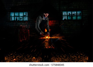The blacksmith manually forging the hot metal on the anvil in smithy with spark fireworks.