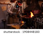 The blacksmith manually forging the molten metal on the anvil in smithy with spark fireworks.