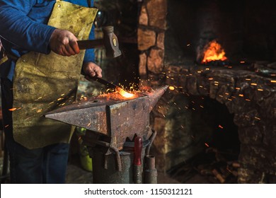 Blacksmith manually forging the molten metal on the anvil in smithy with spark fireworks, close up