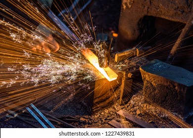 Blacksmith manually forging the molten metal on the anvil with spark fireworks