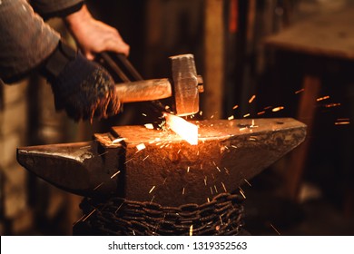 The blacksmith manually forging the red-hot metal on the anvil in smithy with spark fireworks