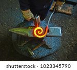 Blacksmith is processing a hot metal object of a spiral shape at anvil in a workshop