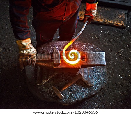 Blacksmith is processing a hot metal object of a spiral shape at anvil in a workshop