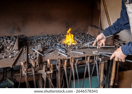 Blacksmith skillfully using metal pliers to grip a glowing piece of iron over burning coal in a traditional forge, surrounded by various tools hanging within the workshop