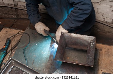 Blacksmith soldering metal plates to a metal stand with ornament. The blacksmith in white blacksmith gloves soldering metal stand in workshop - Powered by Shutterstock