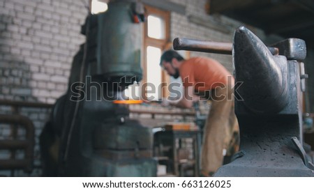 Blacksmith substitutes a metal piece for an automatic hammer