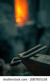 Blacksmith Tongs Lie On An Anvil, In The Background A Fire In A Forge. Forge.