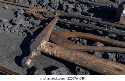 Blacksmith Tools For Hand Forging. Hammer And Tongs On An Iron Surface Among Coke