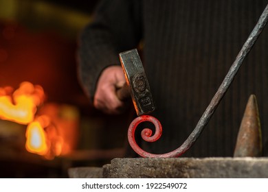 The blacksmith twists the spiral with a sledgehammer, placing a red-hot iron blank on the anvil. Work in the forge