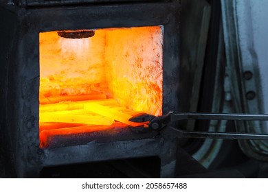 Blacksmith using tongs pulls out a red-hot part metal piece from heated furnace. Pile of hot steel parts in a forge furnace - Powered by Shutterstock