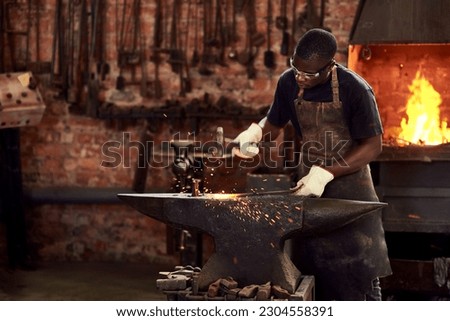Blacksmith, worker and metal forge in workshop and manual industry working on hot steel with hammer, sparks or fire. Black man, welding or iron tools manufacturing or expert, trade and dark workspace
