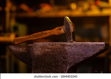 A blacksmith's hammer lying on an anvil in a dark forge. Blacksmithing tools