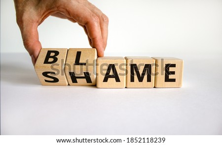 Blame or shame. Male hand flips wooden cubes and changes the inscription 'shame' to 'blame' or vice versa. Beautiful white background, copy space.