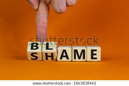 Blame or shame. Male hand flips wooden cubes and changes the word 'shame' to 'blame' or vice versa. Beautiful orange background, copy space. Blame or shame concept.