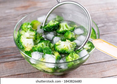Blanched broccoli cabbage cooling down in icy water in a bowl on wooden table - Shutterstock ID 1843826680