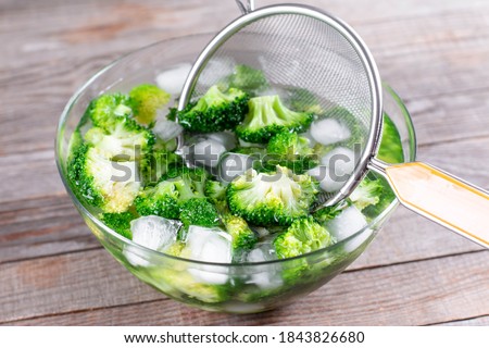 Blanched broccoli cabbage cooling down in icy water in a bowl on wooden table