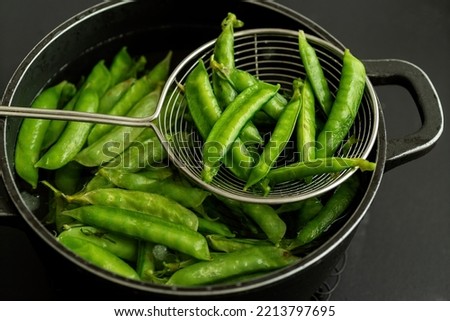Blanched pea pods in a pot with a colander