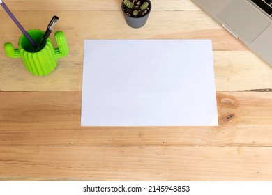 Blank A4 Paper Laying Horizontally On A Wooden Table With Supplies